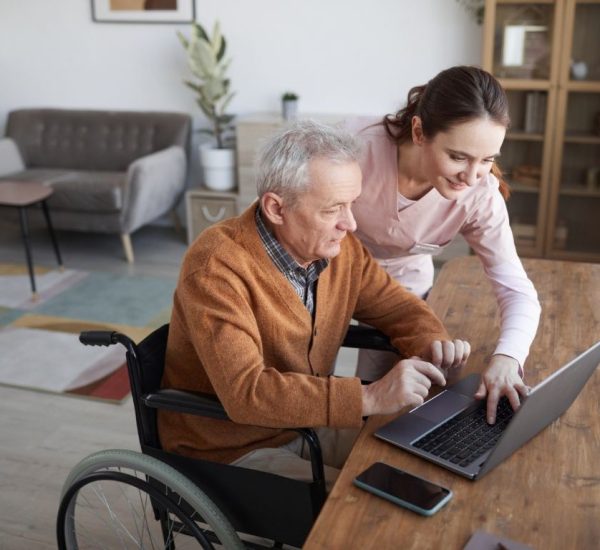a care giver from direct caregiving showing an elderly man something on the laptop